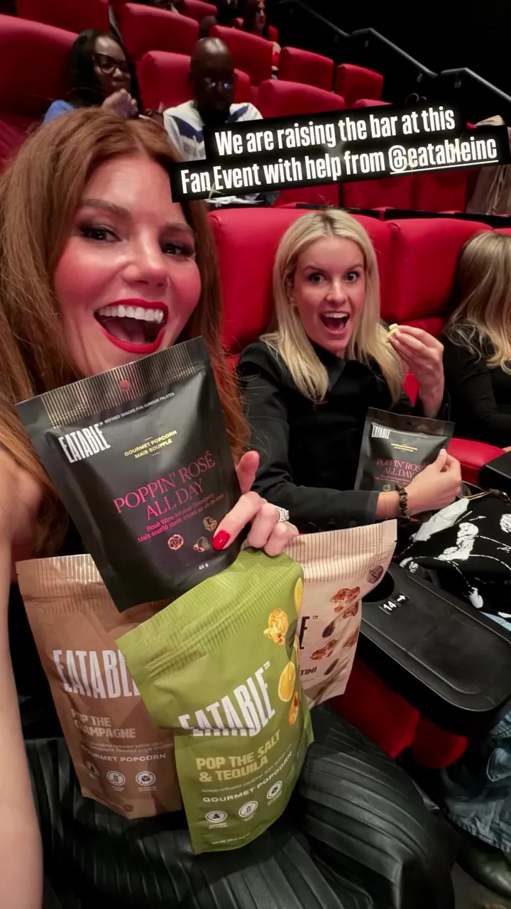 Kristin and a friend in red theater seats with bags of Eatable popcorn